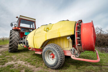 Tractor with agricultural sprayer machine with large fan ready to spray insecticide or pesticide in orchard agriculture concept back view