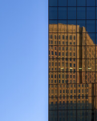 Split perspective of a clear blue sky and the mirrored glass exterior of a modern skyscraper reflecting another nearby building