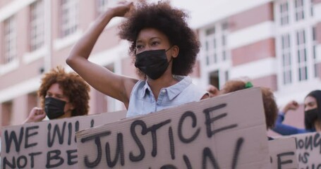 Diverse group of men and women holding placards shouting raising fists during protest wearing masks - Powered by Adobe