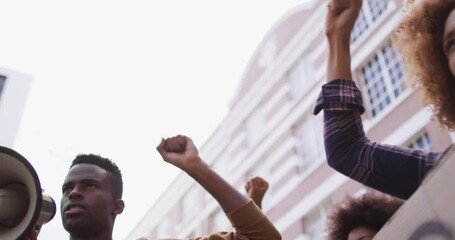 African american man shouting using megaphone with other people raising fists during protest