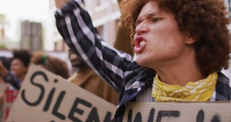 Diverse group of men and women holding placards shouting raising fists during protest