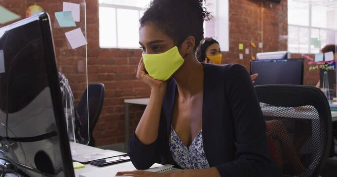 Mixed race businesswoman having video chat sitting in front of computer wearing face mask