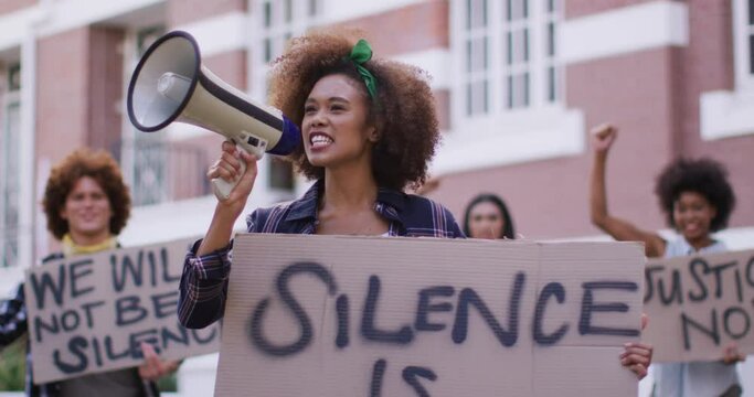 Diverse group of men and women holding placards shouting using megaphone during protest
