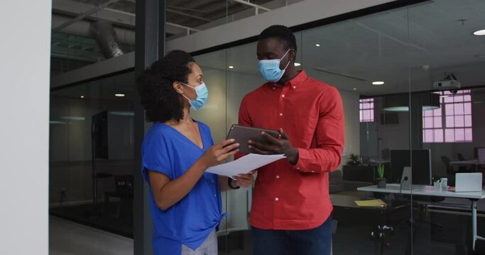 Diverse race male and female business colleagues wearing face masks discussing over tablet