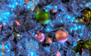 Fototapeta na wymiar Close-up view of a number of colorful Christmas ornaments on a blue Christmas tree, illuminated by blue lights