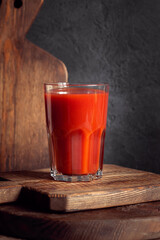 Fresh tomato juice in glass with drinking straw on old wooden board on grey rustic background