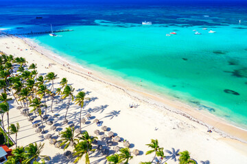 Aerial drone view of beautiful caribbean tropical beach with straw umbrellas, palms and boats....