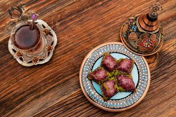 Closeup of traditional Turkish dessert - baklava (violet baklava) on wooden background. Most popular dessert in Ramadan time (Turkish: Ramazan bayrami). Traditional Turkish tea in glass cup. Top view.