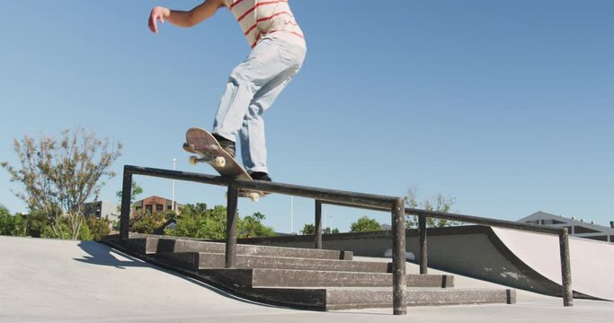Low section of caucasian man riding and jumping on skateboard on sunny day