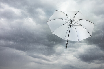 White umbrella blowing away in dark cloudy sky on windy and rainy storm day, depth of field. Scene of heavy rain and dramatic clouds with parasol fly over. Climate concept, abstract background.