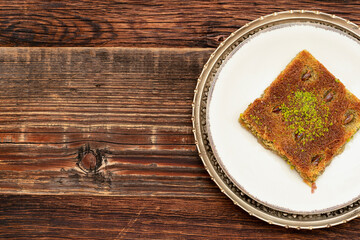 Closeup of traditional Turkish dessert - Kadayif with pistachio powder (Burma kadayif) on wooden background. Most popular dessert in Ramadan time (Turkish: Ramazan bayrami).