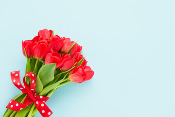 Red tulips bouquet decorated with ribbon on a blue background. Mothers Day, Valentines Day, birthday celebration concept