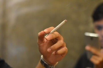 the gesture of a male hand holding a cigarette against a wooden background