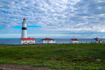 Point Amour Historic Lighthouse on the edge of the Atlantic Ocean. The blue sky is hidden by fluffy...