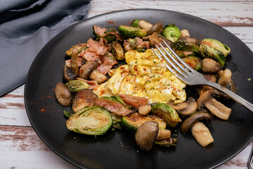 Plate of Brussels sprouts with portobellos and mushrooms with bacon and scrambled eggs. Picado point of view.