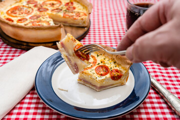 A man's hand holding a piece of ham and cheesecake slice or Quiche Loraine on a fork. Home food, healthy concept