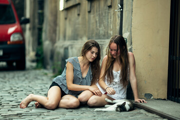 Fototapeta na wymiar Two teenage girls sitting on the pavement with a cat.