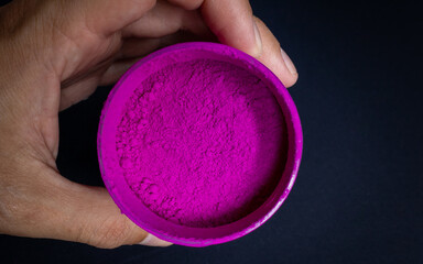 Transparent plastic pot held by the hand of a brown man containing resin powder or pigment on a...