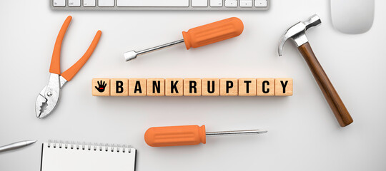 wooden cubes with the message BANKRUPTCY surrounded by handiman tools and office equipment on white...