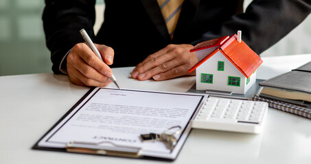 Close up wooden toy house with business woman signs a purchase contract or mortgage for a home,...