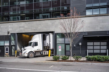 Big rig day cab semi truck with refrigerator semi trailer make a delivery to local store in multilevel apartment building