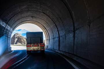 Loaded big rig semi truck with flat bed semi trailer transporting cargo driving on the winding road through a arched tunnel in the rock at Columbia River Gorge