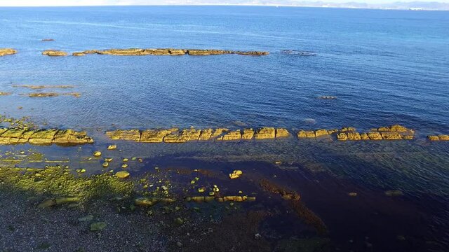 Aerial view of the sea side. Some rocks perfectly aligned on a narrow row are seen. Several paralel lines of rocks seen.