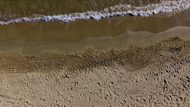 Aerial static view of the sea shore in a beach. Some dry white sands on one side and the small waves coming and going leaving the darker wet sand in between.