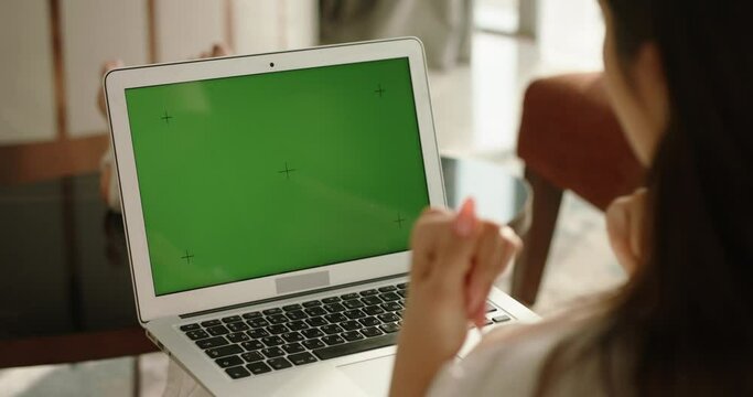 Rear view of girl using a laptop computer with green chroma key mock up screen for video online conference, gesturing with hands 4k footage
