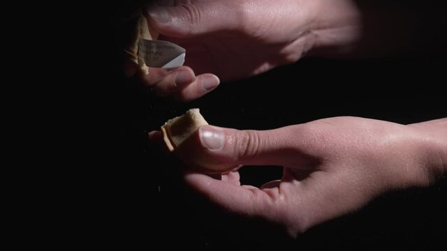 This video shows hands opening a traditional fortune cookie against a black background.