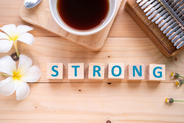Positive Words Vocabulary  concept, STRONG word cube wooden with Coffee mugs, Kalimba and small flowers on the wooden background, start your work day refreshed.