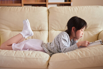 リビングのソファーの上で本を見ている可愛い女の子の様子