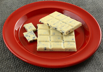 White chocolate bar with bits of chocolate cookies on red snack plate on gray burlap