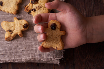 Homemade gluten-free, lactose-free cookies without sugar with raisins and chocolate on dark brown wooden background and Child hand holds gingerbread 