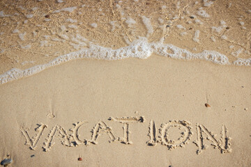 Inscription vacation and incoming sea wave on sand at beach. Summer time