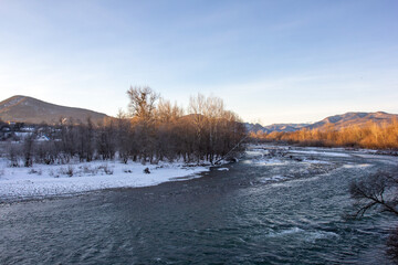 Winter in the foothills, an ice-free river on a frosty morning in the rays of the rising sun.