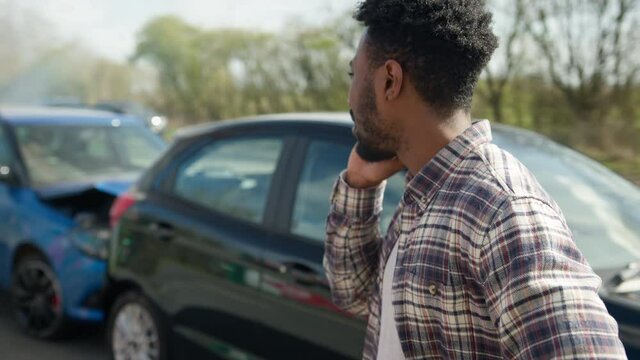 Young Male Driver Calling Car Insurance Company On Mobile Phone After Road Traffic Accident