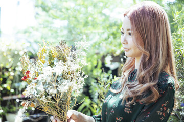 Naklejka premium 植物に囲まれて、ドライフラワーの花束を持つ女性のアップ写真
