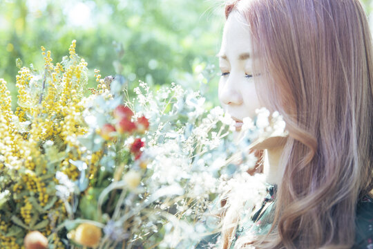 植物に囲まれて、ドライフラワーの花束を持つ女性のアップ写真