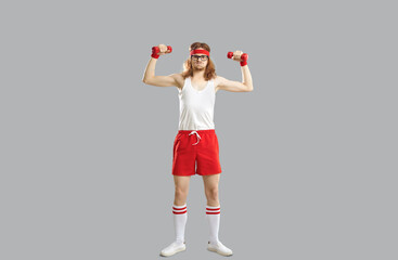 Funny smiling hipster skinny young guy in red and white sportswear standing and doing workout with...