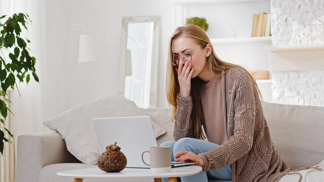 Caucasian millennial woman sitting at home looking at laptop reads bad news receives rejection email makes mistake online error problem loses feels shock desperate closes mouth with hand holding head