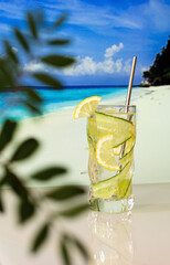 Chilled cocktail with lemon and ice on the background of the beach, blue sea and blue sky
