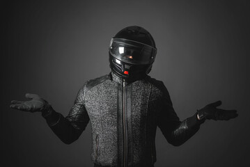 Confused motorbiker is shrugging shoulders and spreading hands on a dark background....