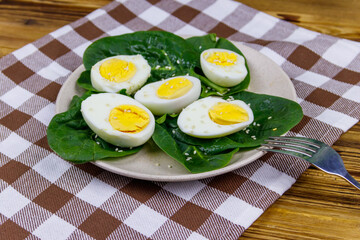 Boiled eggs with fresh spinach leaves and sesame seeds on wooden table
