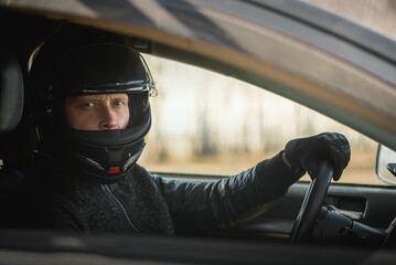 Rally driver concept. Man in a helmet is sitting by the car steering wheel close up.
