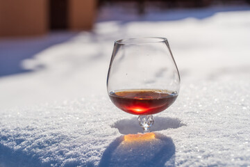 Glass of cognac on a bed of snow and white background, close up