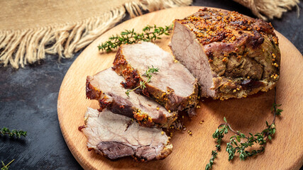 Large sliced piece of baked pork back wwith mustard and thyme on a wooden board. Food recipe background. Close up