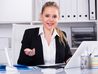 Smiling woman sitting at table and working on laptop in office