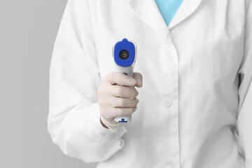 Doctor with infrared thermometer on grey background, closeup