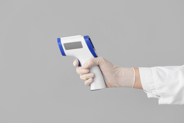 Hand of doctor with infrared thermometer on grey background